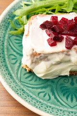 Top view of blue plate with cod pudding with mayonnaise, beetroot chunks and arugula on wooden table, selective focus, vertical