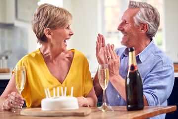 Retired Couple Celebrating Birthday With Glass Of Champagne And Cake At Home Together