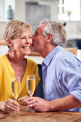 Kissing Retired Couple Celebrating With Glass Of Champagne At Home On Date Night Together