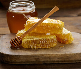 wax honeycomb with honey on a wooden board, behind a jar of honey