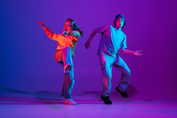 Two dancers, young man and woman dancing hip-hop in casual sports youth clothes on gradient purple...