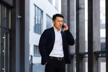 angry and serious Successful Asian businessman explains information to employees using phone, speaks near office outside