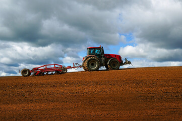 Close-up of agriculture red tractor cultivating field over blue sky with clouds