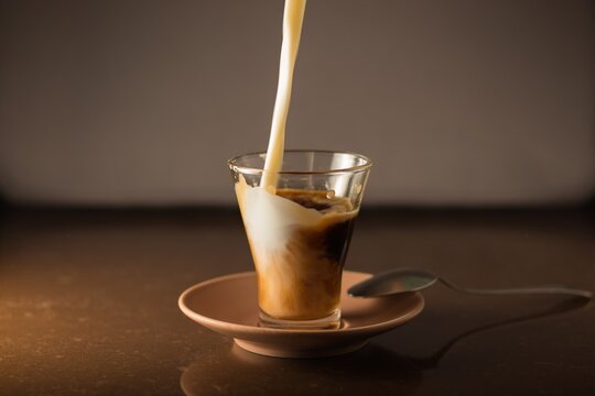 chorro de leche cae desde arriba entrando dentro de la taza de caf&eacute; para hacer caf&eacute; con leche con un ambiente c&aacute;lido y tranquilo