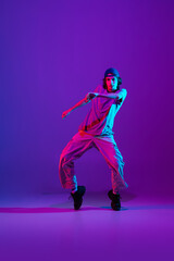 Fototapeta na wymiar Young stylish man, break dancing, hip-hop dancer practicing solo in casual clothes isolated over purple background in neon pink light at dance hall