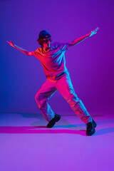 Sportive young man dancing hip-hop in stylish clothes on colorful background at dance hall in neon light. Youth culture, movement, style and fashion, action.