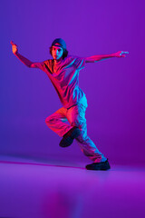 Fototapeta na wymiar Stylish sportive boy dancing hip-hop in stylish clothes on colorful background at dance hall in neon light. Youth culture, movement, style and fashion, action.