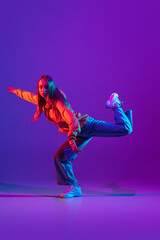 Stylish sportive girl dancing hip-hop in stylish clothes on colorful background at dance hall in neon light. Youth culture, movement, style and fashion, action.