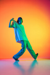 Conceptual portrait of young man, hip-hop dancer in stylish clothes in action isolated on colorful background at dance hall in neon light.