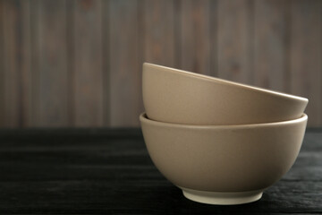 Stylish empty ceramic bowls on black wooden table, space for text. Cooking utensils