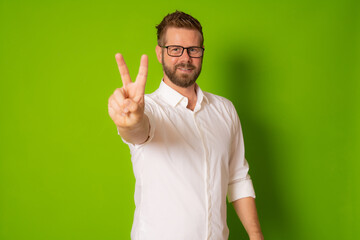 Fototapeta premium Handsome young man with beard wearing shirt smiling looking to the camera showing fingers doing victory sign.