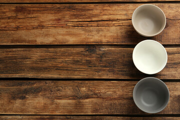 Stylish empty ceramic bowls on wooden table, flat lay and space for text. Cooking utensils