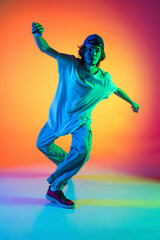 Close-up portrait of young man, hip-hop dancer in stylish clothes in action isolated on colorful background at dance hall in neon light.