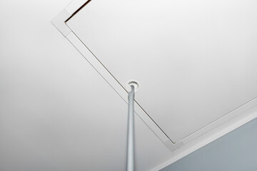 Folding metal stairs to the attic in the ceiling, closed hatch with a tube for opening, modern look.