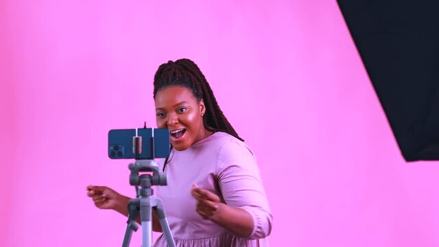 dark skinned woman laughing and shooting social media stories in pink wall background