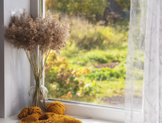 On the window the process of knitting and a bouquet of dry branches of grass. The concept of autumn and needlework.