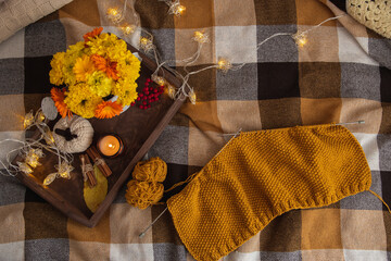 View from above of the cozy atmosphere of home crafts. On a plaid blanket knitting process, a wooden tray with decor: candle, autumn bouquet, garland.