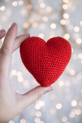 Knitted red heart in the hand against the background of a garland. The concept of love and Valentines Day.