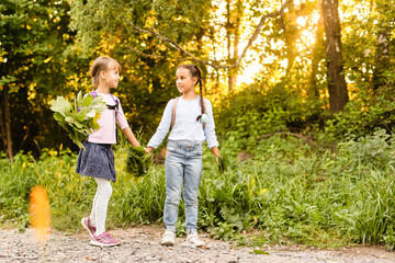 Fototapeta premium Two girls are having fun in the park, autumn outfit. Funny girl friends throwing leaves in the city in autumn. Happy family on autumn walk. Geasture peace.