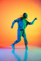 Fototapeta na wymiar Young sportive girl dancing hip-hop in stylish clothes on colorful background at dance hall in neon light. Youth culture, movement, style and fashion, action.