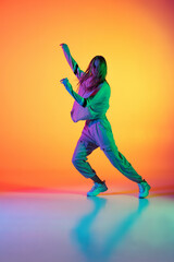 One Caucasian sportive girl dancing hip-hop in stylish clothes on colorful background at dance hall in neon light. Youth culture, movement, style and fashion, action.
