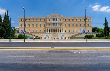 Greek Parliament in Athens, with the Greek flag blowing in the wind, on a sunny day - obrazy, fototapety, plakaty