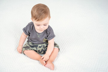 Fototapeta premium Caucasian baby boy in a khaki shorts sitting on bed in room. View from top above. Healthy childhood lifestyle.