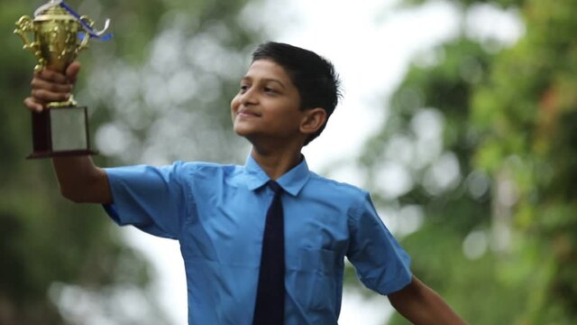 Clever schoolboy raising his trophy as a winner in school competition.