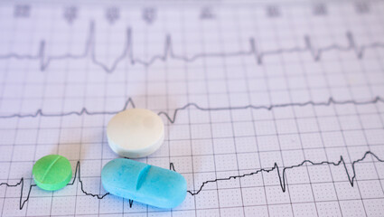 Closeup to two colored pills on an electrocardiogram paper with cardiac arrhythmia. Long COVID disease concept.