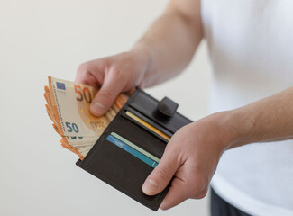 Pay in euros. Get euros from your wallet. Male  hands holding a black leather wallet with 50 euro banknotes and counting them. - obrazy, fototapety, plakaty