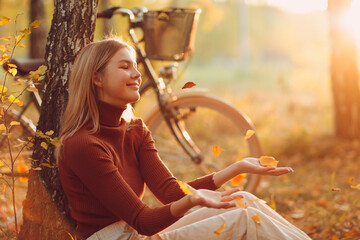 Happy young woman sitting near vintage bicycle in autumn park at sunset. Fall season concept.