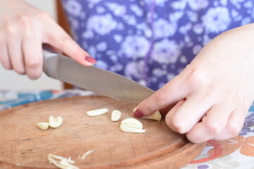 a woman chopping pieces of garlic on a wooden board
