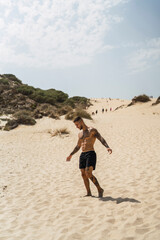 Chico atletico tatuado posando en dunas de arena