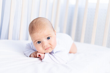 cute newborn baby on tummy in crib on cotton bed at home, healthy sleep concept