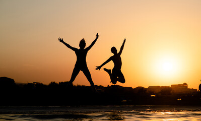 Fototapeta premium Happy friends are having fun and jump at sunset beach in sunlight. Empty space for text