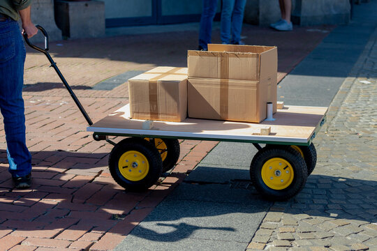 Luggage trolley with 4 wheels with brown boxes on street in city, Service deliver carrying packages to delivery to customer with low angle of peoples. - Powered by Adobe