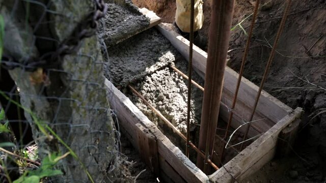 Concrete mixer truck gutter along which liquid flows concrete mixture into the formwork with rebar and worker do the foundation. Retaining wall. Fence. Close-up. Transporting tank. Building process.