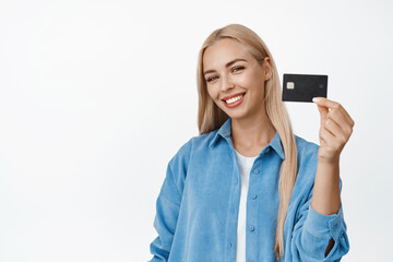 Beautiful blond woman smiling, showing her credit discount card, standing in casual clothes over white background