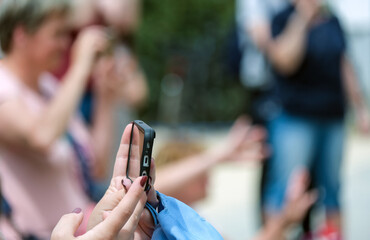 Frau fotografiert und filmt in einer Gruppe mit ihrem Smartphone bei einer öffentlichen...