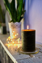 Brennende Kerze mit Lichterkette und Pflanze im Hintergrund