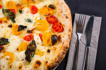 Pizza napoletana con pomodorini gialli e rossi, mozzarella di bufala e basilico fresco fotografata dall'alto su uno sfondo nero