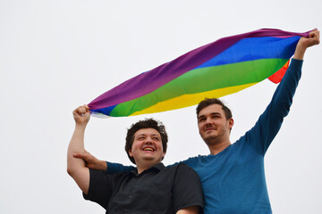 Two beautiful men hold the LGBT pride flag.