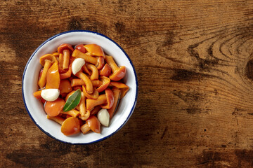 Pickled mushrooms with garlic and a bay leaf, overhead shot on a dark rustic wooden background with copy space