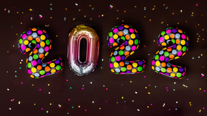 Colorful balloons with multicolored polka dots in form of numbers 2022 with colorful shiny confetti on black background. Happy New Year celebration. Flat lay, top view