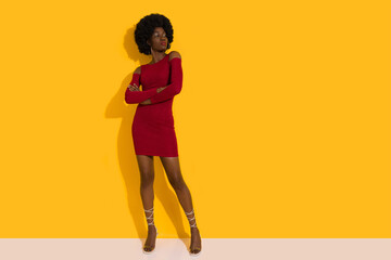 Fototapeta na wymiar Confident Young Black Fashion Model In Red Mini Dress And High Heels Is Posing With Arms Crossed