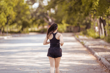 Happy smiling adult Asian woman jogging outdoor in the city park in sunshine beautiful summer day.  Happy relaxed mature woman jogging to live an active and healthy lifestyle