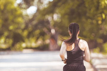 Happy smiling adult Asian woman jogging outdoor in the city park in sunshine beautiful summer day.  Happy relaxed mature woman jogging to live an active and healthy lifestyle