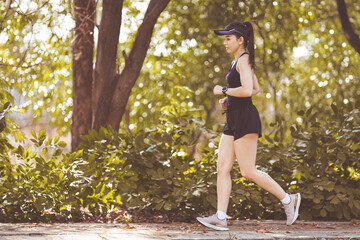 Happy smiling adult Asian woman jogging outdoor in the city park in sunshine beautiful summer day.  Happy relaxed mature woman jogging to live an active and healthy lifestyle