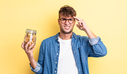 young handsome man feeling confused and puzzled, showing you are insane. cookies bottle concept