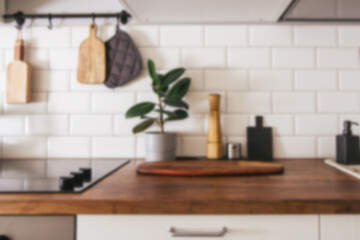 Kitchen brass utensils, chef accessories - blurred kitchen background . Hanging kitchen with white tiles wall and wood tabletop.Green plant on kitchen background